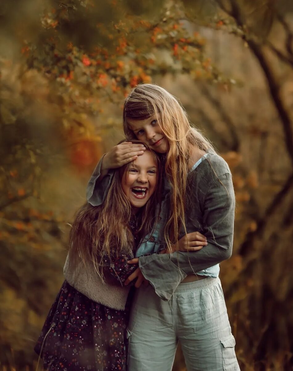 Geschwisterfotografie – zwei Mädchen umarmen sich lachend