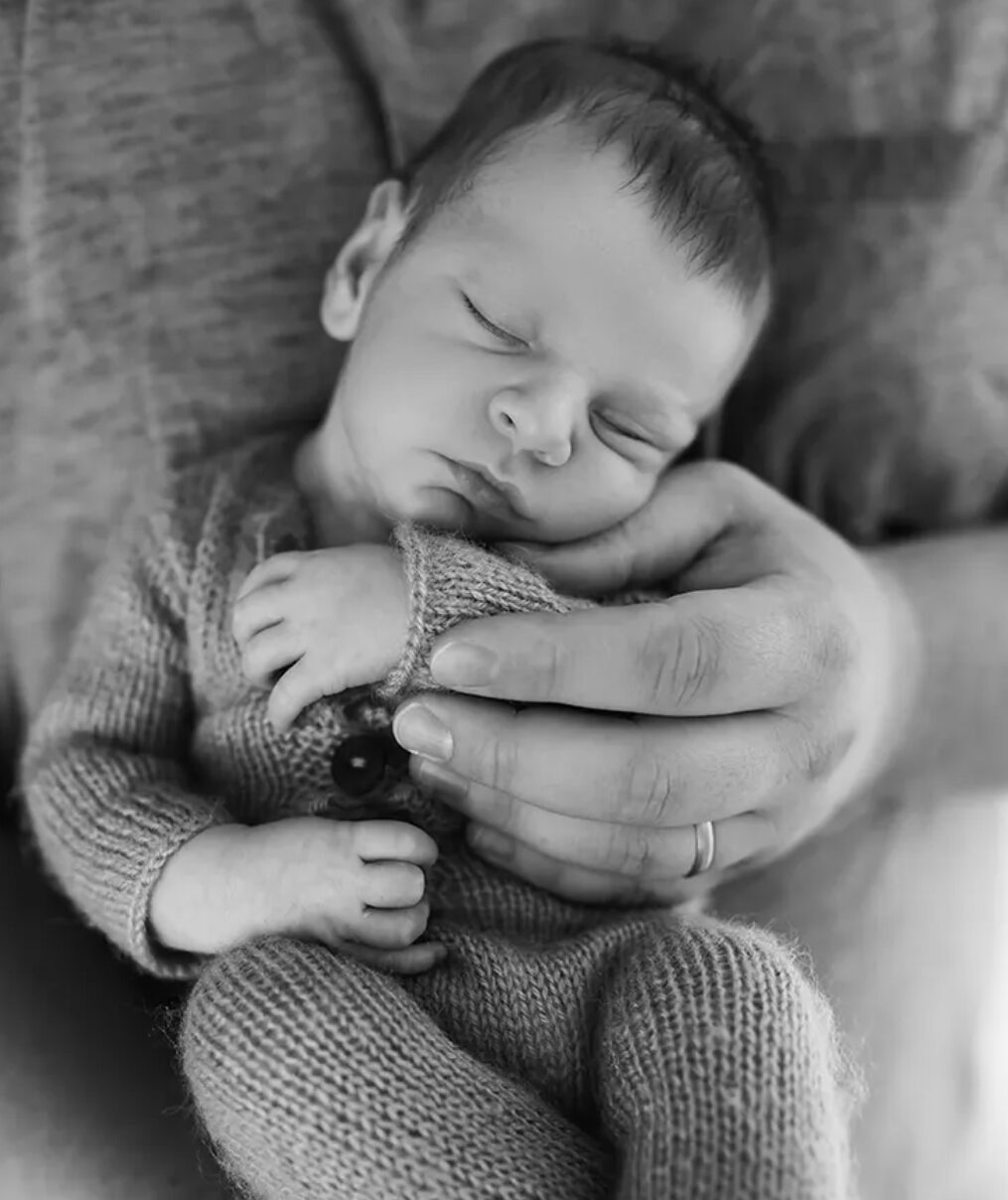 Neugeborenenshooting – Baby auf Papas Arm, schwarz-weiß