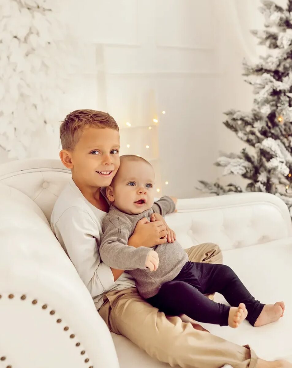 Weihnachts-Mini – Geschwister auf weißem Sofa vor Schneetanne